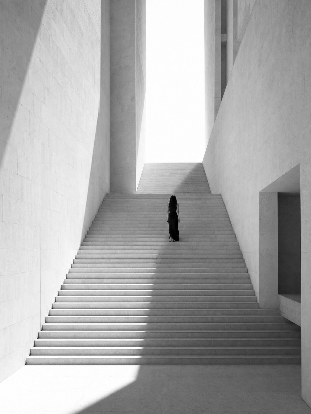 Eine Frau geht eine weiße Treppe hinauf ins Licht